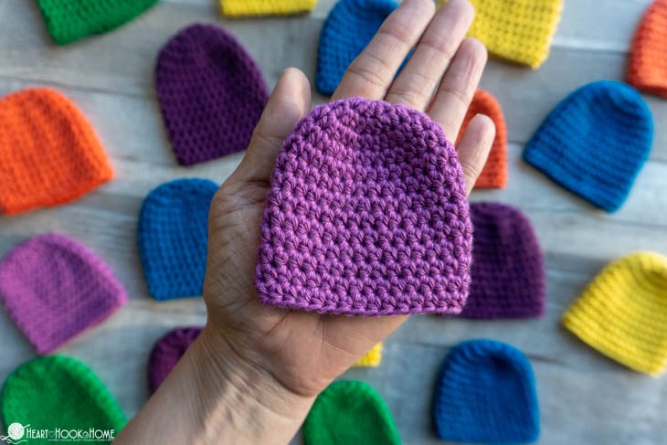 Multiple colors of the Preemie Baby Beanie crochet pattern and a lavender example in an adult\'s hand.