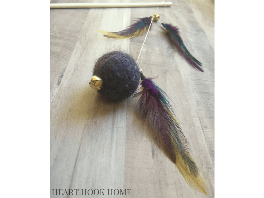 Cat toy made out of a felted yarn ball and feathers with a bell and string.