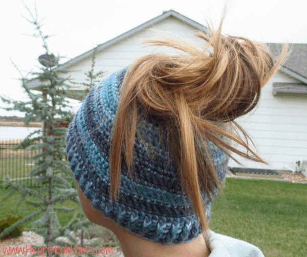 Multi-blue colored example of the Messy Mom Bun Beanie crochet pattern with a brunette ponytail coming out of the top.