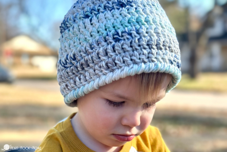 Blue variegated example of the Child Size Easy 30-Minute Beanie crochet pattern on a smiling male child. 