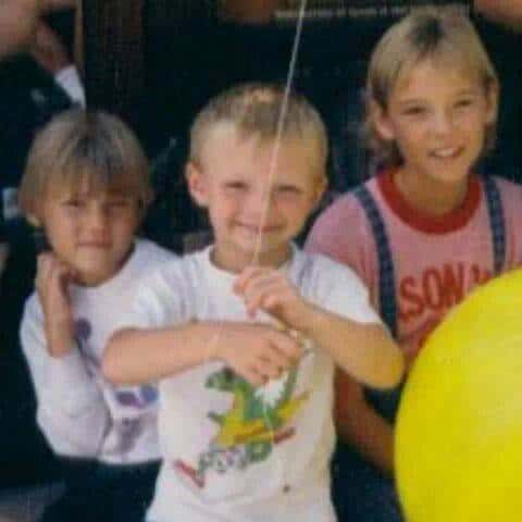 Three blonde siblings smiling for a camera in the 1980\'s.