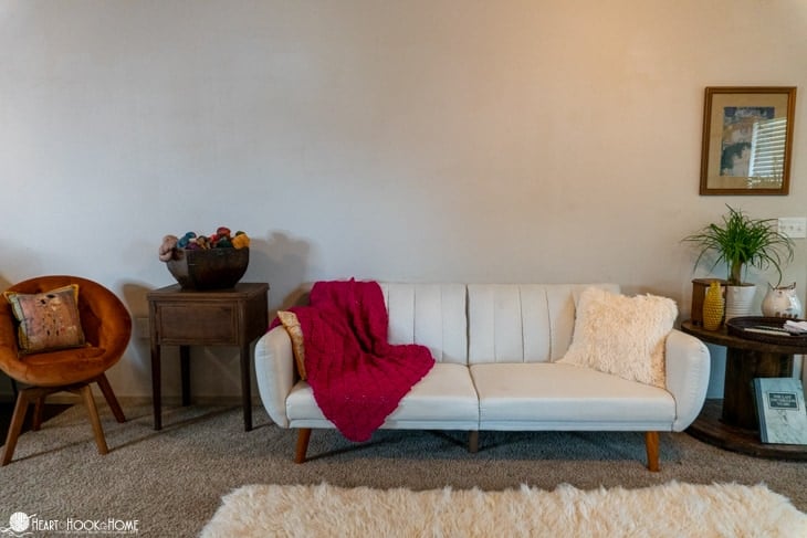White couch with a dragonfruit colored example of a Sangria Sorbet Crochet Blanket pattern draped over it with a white furry rug in the foreground.