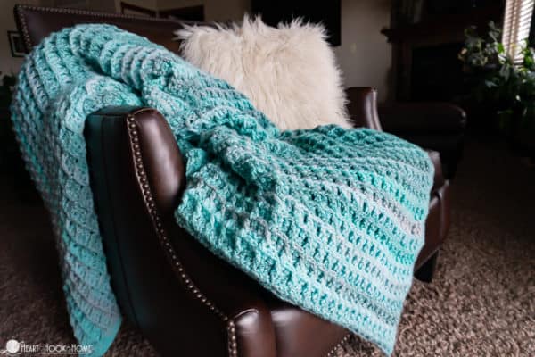 Waffle Blanket in shades of blue draped over a leather chair with a furry throw pillow.