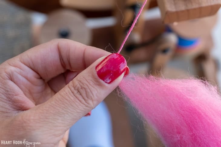 Fingers with red nail polish holding pink roving yarn.