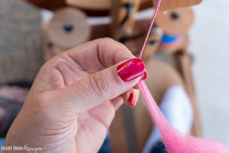 Fingers with red nail polish holding pink roving yarn.
