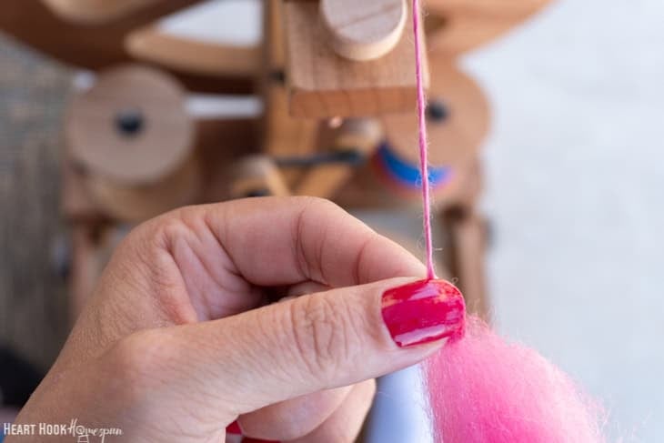 Fingers with red nail polish holding pink roving yarn.