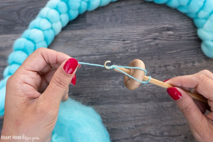 Braid of blue roving yarn and a wood drop spindle with one hand twisting the yarn and the other holding the drop spindle.