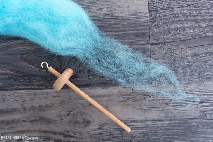Blue roving yarn and a wood drop spindle.