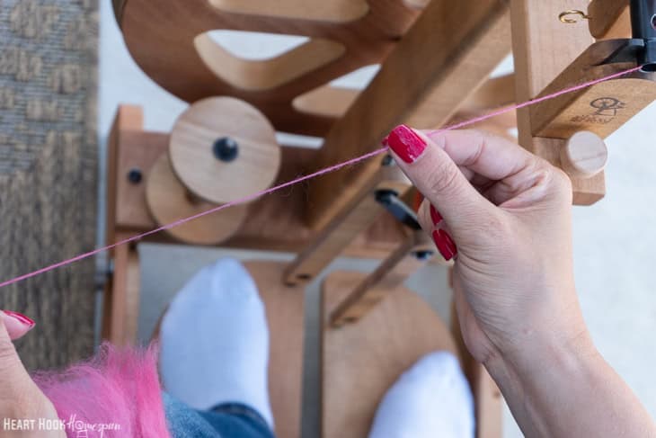 Pink, handspun yarn with a spinning wheel and a pair of legs in the background.