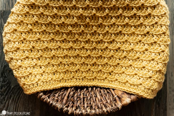 Mustard colorway of an example of the Brick Stitch Cloth crochet pattern laying on a wicker basket.