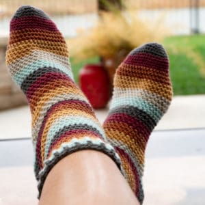 Modeled on a pair of crossed feet is an example of the Herringbone Socks crochet pattern in striped fall colors.