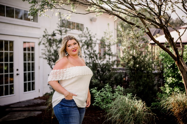 Example of The Vanilla Dreamboat crochet pattern on a smiling female model wearing jeans and standing in a garden setting.