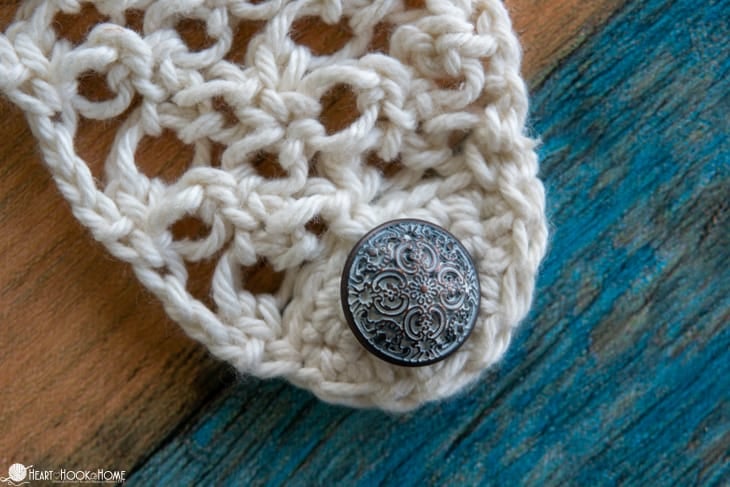 Decorative button on a white colorway sample of the headband style option of the Solomon\'s Hair Net crochet pattern.