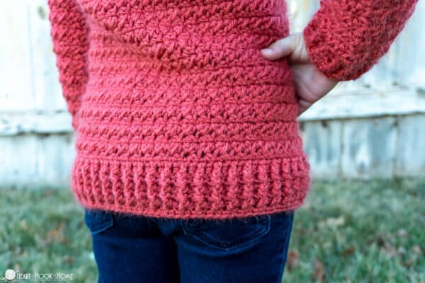 Up close picture of the back side and bottom edging of a pink version of the child size Color Block Sweater crochet pattern on a child.
