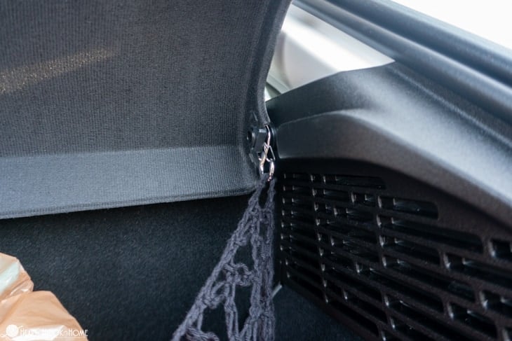 Up close of a carabiner hooked into the corner of the Trunk Cargo Net crochet pattern and attached to the rings in the trunk of a vehicle.