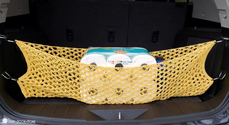 Example of a yellow version of a Trunk Cargo Net crochet pattern installed inside of a vehicle with toilet paper being secured inside of its fold.