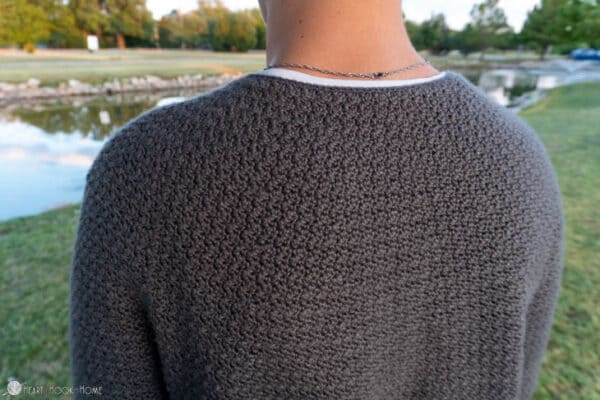 Up close of a Gray colorway of a Denzel Sweater Crochet Pattern on a male model in a park setting.