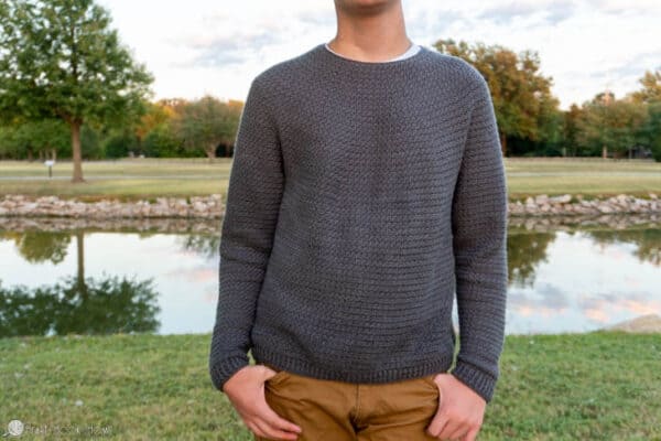 Gray colorway of a Denzel Sweater Crochet Pattern on a male model in a park setting.
