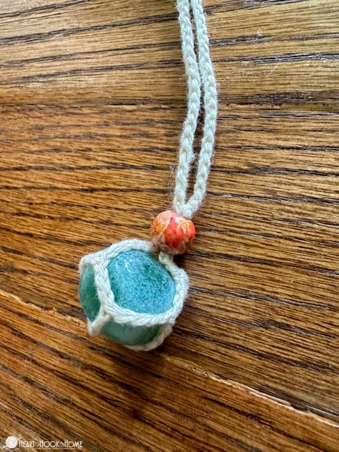 Turquoise colored stone wrapped up in the Gemstone Holder crochet pattern with an orangish colored bead. 