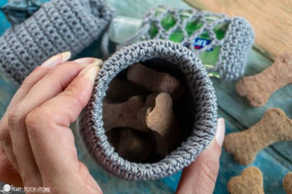 Gray colorway of an example of the Dog Treat Bag crochet pattern with dog treats inside and being held open by a hand.