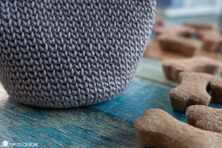 Up close of a gray colorway of an example of the Dog Treat Bag crochet pattern with dog treats sitting next to it.