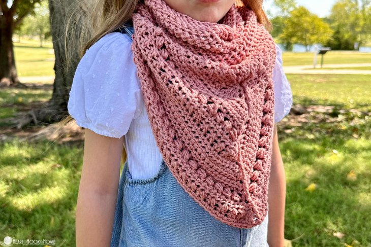 Female child wearing a light blue denim dress and a Lion Brand Coboo yarn in the “mauve” colorway example of the Frankie Cowl crochet pattern in a park setting.