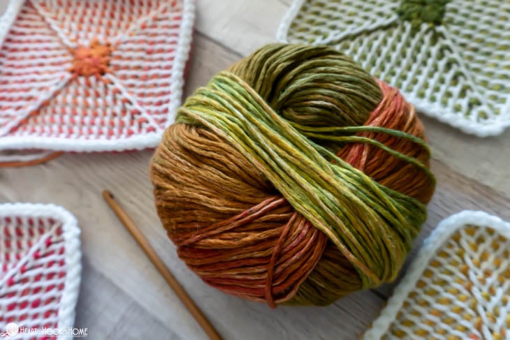 Multiple colored examples of the Tunisian Crochet Granny Square pattern, a multi colored ball of yarn, and a wood crochet hook.